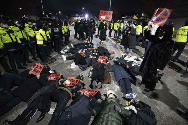 Protesters lie down on the road to oppose the release of Cho Doo-soon in front of a prison in Seoul, South Korea, Saturday, Dec. 12, 2020. Angry protesters threw eggs and shouted insults as Cho, one of South Korea's most notorious child predators, was released from a prison in southern Seoul on Saturday at the end of a 12-year term. The signs read: "Let's castrate Cho Doo-soon." (Yun Dong-jin/Yonhap via AP)