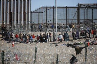Migrantes formados después de ser detenidos por las autoridades migratorias de Estados Unidos en el muro fronterizo, el miércoles 27 de diciembre de 2023, en una imagen captada desde Ciudad Juárez, México. (AP Foto/Christian Chavez)