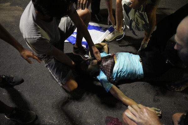 An injured demonstrator is helped after being hurt during clashes with riot police during a protest against plans by Netanyahu's government to overhaul the judicial system, in Tel Aviv, Monday, July 24, 2023. Israeli lawmakers on Monday approved a key portion of Prime Minister Benjamin Netanyahu's divisive plan to reshape the country's justice system despite massive protests that have exposed unprecedented fissures in Israeli society. (AP Photo/Ariel Schalit)