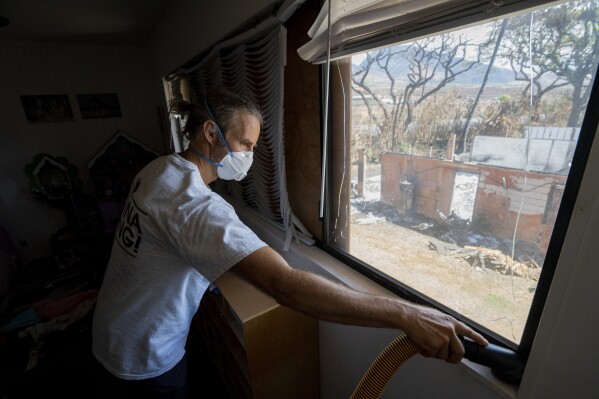 Daniel Skousen vacuums his home, damaged by August's wildfire, on Friday, Nov. 3, 2023, in Lahaina, Hawaii. Skousen stated he will not deep clean his home until the EPA removes all debris from the burnt house adjacent to his. (AP Photo/Mengshin Lin)