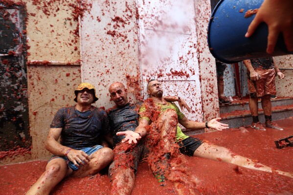 People react during the annual tomato fight fiesta called" Tomatina" in the village of Bunol near Valencia, Spain, Wednesday, Aug. 30, 2023. Thousands gather in this eastern Spanish town for the annual street tomato battle that leaves the streets and participants drenched in red pulp from 120,000 kilos of tomatoes. (AP Photo/Alberto Saiz)