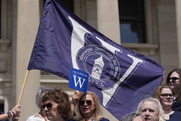 Mississippi University for Women alumni wave their school's flag on the steps of the Mississippi State Capitol, Tuesday, March 12, 2024, in Jackson, as they gather to have group photograph taken in recognition of the Columbus, Miss., based school's 140th anniversary of the school's charter -- and also to voice their opposition to a bill to merge the university with Mississippi State University. (AP Photo/Rogelio V. Solis)