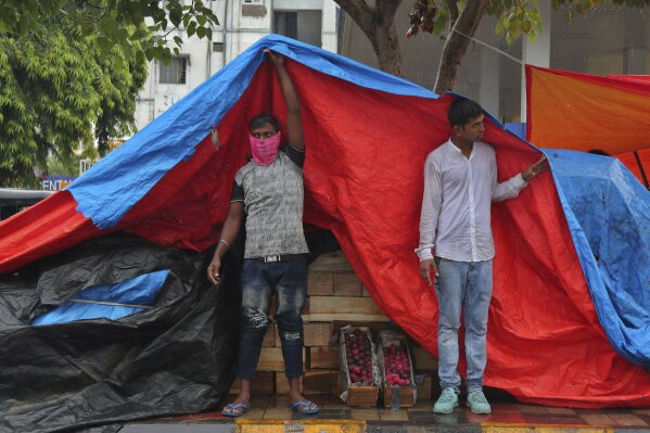 An Indian fruit vendor wearing face mask to protect from the coronavirus uses a plastic sheet to cover from rain in Hyderabad, India, Thursday, July 23, 2020. India receives its monsoon rains from June to September. (AP Photo/Mahesh Kumar A.)