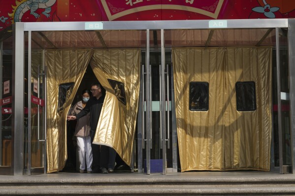 People walk out from a shopping mall in Beijing, China, Friday, April 5, 2024. (AP Photo/Tatan Syuflana)