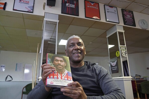 Former England international soccer player Ricky Hill poses with a copy of his book for a photograph in Luton, England, Wednesday, March 20, 2024. Racism has long permeated the world’s most popular sport, with soccer players subjected to racist chants and taunts online. While governing bodies like FIFA and UEFA have taken steps to combat the abuse of players, the lack of diversity in the upper ranks at major clubs remains an unsolved problem. Hill has just left the U.K. to take a management position with a suburban Chicago soccer club. (AP Photo/Kin Cheung)