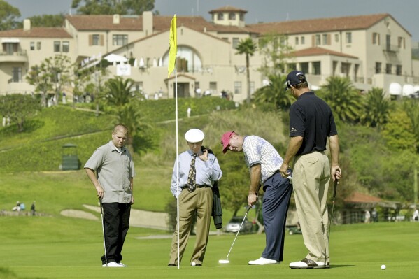 FILE - With the historic clubhouse in the background, Duffy Waldorf takes a practice putt at the 10th green as veteran teaching pro Eddie Merrins, in the tie, and golfer Arron Oberholser, right, watch during a practice session for the Nissan Open at Riviera Country Club, Feb. 18, 2003, in Los Angeles. Merrins died Wednesday, Nov. 22, 2023, at age 91. (AP Photo/Reed Saxon, File)