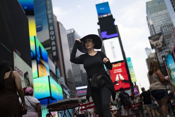 FILE - Pedestrians cover themselves as they pass through Times Square while temperatures rise, July 27, 2023, in New York. Human-caused global warming made July hotter for four out of five people on Earth, according to a new report issued Wednesday, Aug. 2, 2023, by Climate Central. (AP Photo/John Minchillo, File)