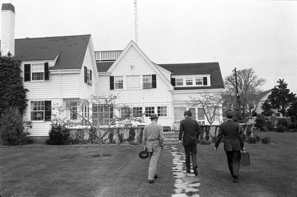 In this photo obtained by the National Security Archive from the John F. Kennedy Presidential Library, White House military aide Gen. Chester Clifton carries the Presidential Emergency Satchel with Kennedy and David Powers, approaching the "cottage" at Hyannis Port, Mass., on May 10, 1963, where Kennedy met with Canadian Prime Minister Lester Pearson. (John F. Kennedy Presidential Library/National Security Archive - nsarchive.gwu.edu via AP)