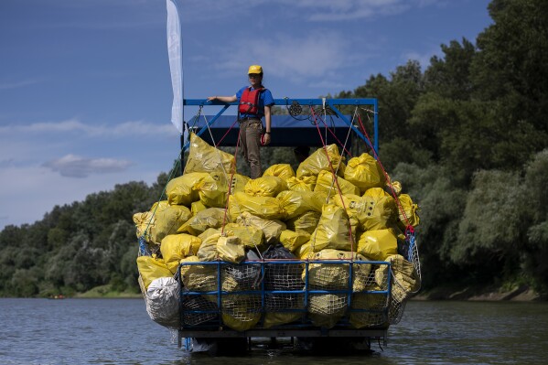 A volunteer stands on top of a pile of rubbish collected that day while participating in the Plastic Cup event near Tiszaroff, Hungary, Wednesday, Aug. 2, 2023. Life-jacketed rivergoers of all ages pile into dozens of canoes to scour Hungary’s second-largest river for trash that has flowed downstream. (AP Photo/Denes Erdos)