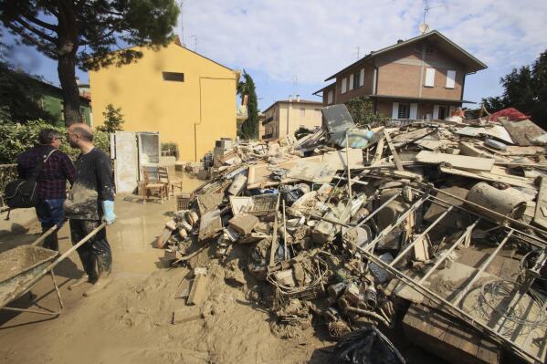 FILE - Volunteers clear mud as household goods are piled on the side of a street in Faenza, Italy, Monday, May 22, 2023. The Italian government has approved more than 2 billion euros ($2.2 billion) in aid for the flood-stricken region of Emilia-Romagna in the north. Premier Giorgia Meloni said the assistance approved at a Cabinet meeting on Tuesday, May 23, 2023 includes suspension of tax and mortgage payments through August for those who suffered flood damage. (Michele Nucci/LaPresse via AP, File)