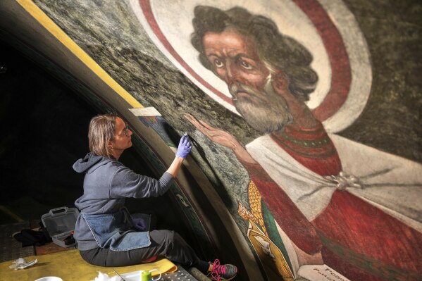Sitting on a 32-foot-tall scaffold, art conservator Cricket Harbeck works on cleaning a mural by Maxo Vanka depicting St. Mark, inside St. Nicholas Croatian Catholic Church in Millvale, Pa., Monday, May 19, 2025. (AP Photo/Gene J. Puskar)