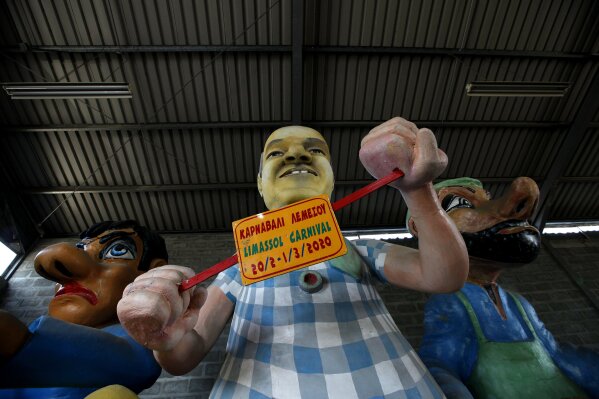 Carnival figures with a sign showing the dates of 2020 carnival celebrations, stacked in a warehouse in southern coastal city of Limassol, Cyprus, Thursday, March 4, 2021. Limassol's municipal authorities aren't letting the festive spirit completely wither away, as they're organizing a series of events conforming to coronavirus health safety protocols, culminating in an outing of King Carnival lead float that marks the theme of the entire period of festivities.(AP Photo/Petros Karadjias)
