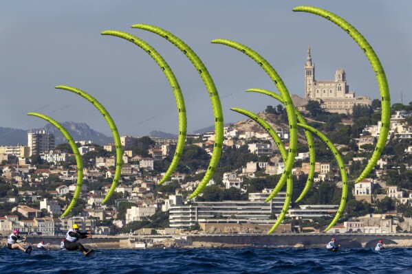 Switzerland's Elena Lengwiler leads the pack, with Marseille's Notre Dame de la Garde Basilica in the background, during a women's kite race, Sunday, Aug. 4, 2024, at the 2024 Summer Olympics in Marseille, France. (AP Photo/Jacquelyn Martin)