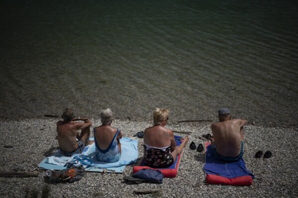 Dutch tourists sunbathe at the Lac de Castillon in southern France, Tuesday, June 20, 2023. Human-caused climate change is lengthening droughts in southern France, meaning the reservoirs are increasingly drained to lower levels to maintain the power generation and water supply needed for nearby towns and cities. (AP Photo/Daniel Cole)