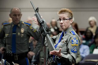 FILE - In this Jan. 28, 2013, file photo, firearms training unit Detective Barbara J. Mattson, of the Connecticut State Police, holds up a Bushmaster AR-15 rifle made by Remington Arms, the same make and model of the gun used by Adam Lanza in the December 2012 Sandy Hook School shooting, during a hearing of a legislative subcommittee in Hartford, Conn. On Tuesday, Aug. 18, 2020, a lawyer for some of the Sandy Hook school shooting victims accused Remington Arms of using its new bankruptcy case to try to wipe out the families' lawsuit against the company over how it marketed the rifle used in the massacre. (AP Photo/Jessica Hill, File)