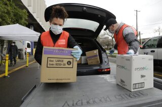 Volunteers Keshia Link, left, and Dan Peterson unload boxes of donated gloves and alcohol wipes from a car at a drive-up donation site for medical supplies at the University of Washington to help fight the coronavirus outbreak Tuesday, March 24, 2020, in Seattle. (AP Photo/Elaine Thompson)