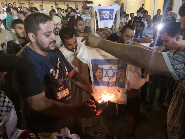 People burn a shirt showing Israeli Foreign Minister Eli Cohen and his Libyan counterpart Najla Mangoush in Tripoli, Libya, Sunday, Aug. 27, 2023. Cohen and Mangoush met in the Italian capital, Rome, last week, according to the Israeli foreign ministry. (AP Photo/Yousef Murad)