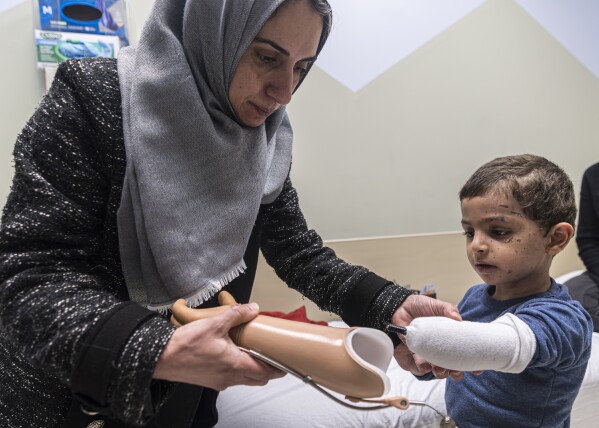 Maha Abu Kuwaik helps her nephew, 4-year-old Omar Abu Kuwaik, attach his new prosthetic arm at Shriners Children's Hospital on Wednesday, Feb. 28, 2024, in Philadelphia. Through the efforts of family and strangers, Omar was brought out of Gaza and to the United States, where he received treatment, including a prosthetic arm. He spent his days in a house run by a medical charity in New York City, accompanied by his aunt. (AP Photo/Peter K. Afriyie)