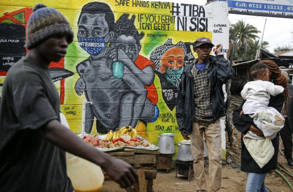 People walk past an informational mural warning people about the dangers of the new coronavirus and how to prevent transmission, with words in Swahili reading "We are the Cure", painted by youth artists from the Uweza Foundation, in the Kibera slum, or informal settlement, of Nairobi, Kenya Wednesday, July 8, 2020. Africa now has more than a half-million confirmed coronavirus cases, according to the Africa Centers for Disease Control and Prevention, but the true number of cases among Africa's 1.3 billion people is unknown as its 54 countries face a serious shortage of testing materials for the virus. (AP Photo/Brian Inganga)