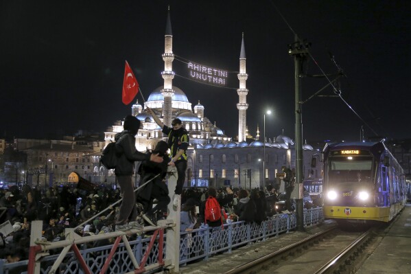 Sinh viên đại học diễu hành qua cầu Galata trong một cuộc biểu tình sau khi Thị trưởng Istanbul Ekrem Imamoglu bị bắt và bị đưa vào tù, tại Istanbul, Thổ Nhĩ Kỳ, Thứ Hai, ngày 24 tháng 3 năm 2025. Đèn trên đỉnh nhà thờ Hồi giáo Yeni có dòng chữ tiếng Thổ Nhĩ Kỳ: "Đừng quên kiếp sau của bạn". (Ảnh AP/Huseyin Aldemir)