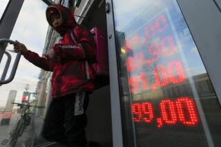 FILE - A food delivery man leaves an exchange office with screen showing the currency exchange rates of U.S. Dollar and Euro to Russian Rubles in Moscow, Russia, Feb. 24, 2022. (AP Photo, File)