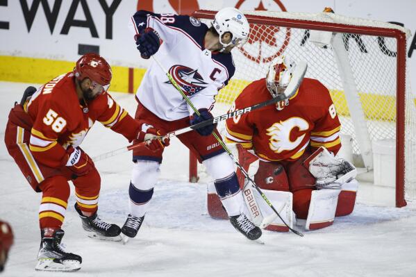 Columbus Blue Jackets' Boone Jenner, center, tries to get the puck past Calgary Flames goalie Jacob Markstrom, right, as Oliver Kylington defends during the first period of an NHL hockey game Tuesday, Feb. 15, 2022, in Calgary, Alberta. (Jeff McIntosh/The Canadian Press via AP)