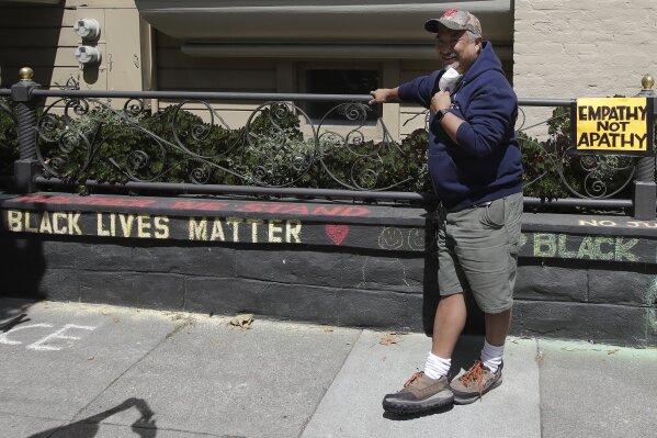 James Juanillo poses next to chalk written outside of his home in San Francisco, Sunday, June 14, 2020. The CEO of a cosmetic company issued an apology Sunday after she and her husband confronted Juanillo and threatened to call police because he stenciled "Black Lives Matter" in chalk on his San Francisco property, as the couple asserted that they know Juanillo doesn’t live there and is therefore breaking the law. (AP Photo/Jeff Chiu)