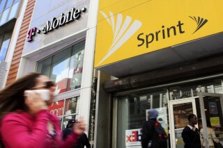 FILE - In this April 27, 2010 file photo, a woman using a cell phone walks past T-Mobile and Sprint stores in New York. T-Mobile, in its attempt to buy Sprint for $26.5 billion, shrinking the major wireless companies to three from four and creating another phone giant to rival AT&T and Verizon, has already notched approvals from federal national-security, telecommunications and antitrust regulators. Now it must convince a federal court judge in New York that the 14 state attorneys general suing to stop its deal are wrong. (AP Photo/Mark Lennihan, File)