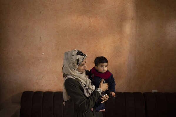 CORRECTS LOCATION - Amal Al-Taweel poses for a photo with her baby Ali at her family home in Nuseirat, central Gaza Strip, Friday, April 5, 2024. Ali was born Oct. 7, the day the Israel-Hamas war erupted. Mothers who gave birth in the Gaza Strip that day fret that their 6-month-old babies have known nothing but brutal war, characterized by a lack of baby food, unsanitary shelter conditions and the crashing of airstrikes. (AP Photo/Fatima Shbair)