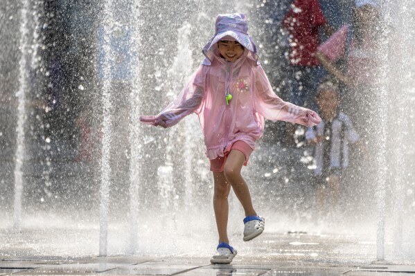 A girl runs as she plays in a fountain at a shopping mall in Beijing, Friday, June 23, 2023. Authorities issued a rare red alert for high temperatures in parts of China's capital on Friday, the highest level of warning, as highs were expected to once again climb to around 40 degrees Celsius (104 degrees Farenheit). (AP Photo/Mark Schiefelbein)