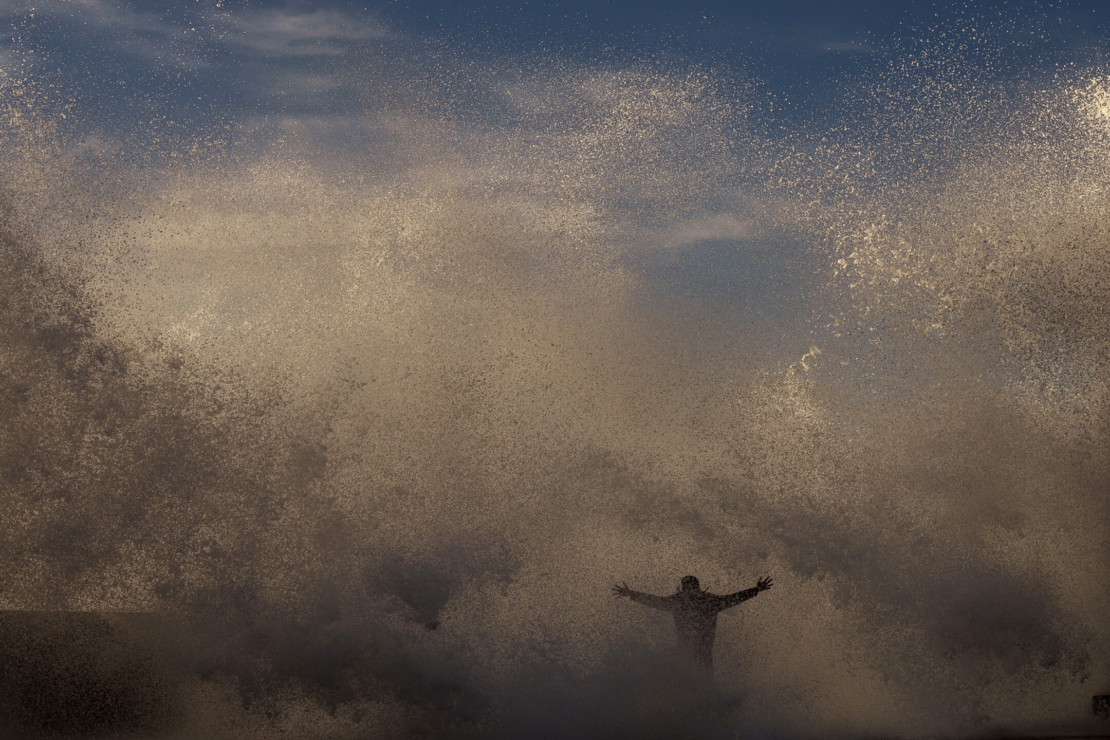 A person stands as a wave crashes against the sea barrier on the promenade of the beach in Rabat, Morocco, on Feb. 9, 2023. (AP Photo/Manu Fernandez)