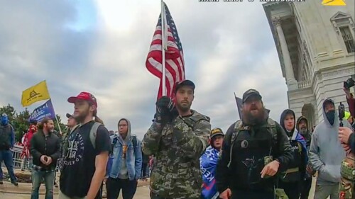 In this image from video provided by the Justice Department in the government's sentencing memo for Christopher Michael Alberts, right, yells at U.S. Capitol Police offices during the Jan. 6, 2021, riot at the U.S. Capitol. Alberts, a military veteran who stormed the U.S. Capitol with a loaded pistol, metal-plated body armor and a gas mask has been sentenced to seven years in prison. (Justice Department via AP)