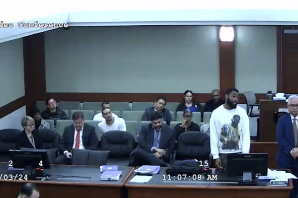 In this image from video provided by the Clark County District Court, defendant Deobra Redden in a white long-sleeved shirt is seen standing next to his defense attorney at his sentencing in a felony battery case, Wednesday, Jan. 3, 2024 in Las Vegas. Redden, who was captured in courtroom video leaping over a judge's bench and attacking her, touching off a bloody brawl, is scheduled to appear before her again Monday morning, Jan. 8, 2024. (Clark County District Court via AP)