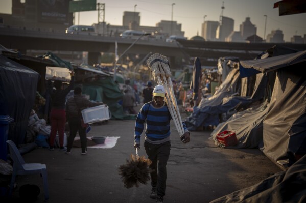A man carries brooms and dusters for sale at a market in downtown Durban, South Africa, Tuesday, May 28, 2024. (AP Photo/Emilio Morenatti)