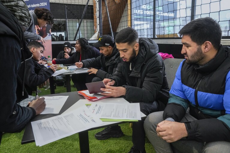 Job seekers fill the papers as they apply for the security jobs during the Olympics jobs fair at sport center in Paris, Thursday, Dec. 14, 2023. Organizers urgently need many thousands of recruits for the huge security operation that will aim to keep athletes and spectators safe during the July 26-Aug. 11 Summer Games in the French capital that has been repeatedly hit by deadly extremist attacks. (AP Photo/Michel Euler)