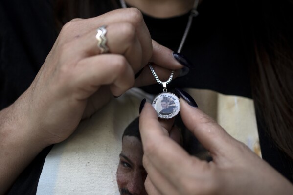 Hagit Chen holds a necklace depicting her son, slain Israeli soldier Itai Chen, in Tel Aviv, Wednesday, May 8, 2024. Itai Chen was killed in a Hamas attack on October 7.  But unlike dozens of other families of soldiers killed that day, Chen's family has no grave to visit because their son's remains are being held in Gaza.  The absence of a final resting place is being felt acutely now, as Israel marks Remembrance Day for Fallen Soldiers, when cemeteries are filled with relatives weeping over the graves of their loved ones.  (AP Photo/Maya Aleruso)