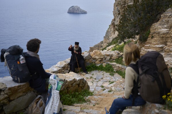 O monge cristão ortodoxo Padre Spyridon fala com o casal francês recém-casado Thomas e Valentine a caminho do Mosteiro de Panagia Hozoviotissa na ilha de Amorgos, Grécia, na terça-feira, 25 de março de 2025. (Foto AP/Petros Giannakouris)