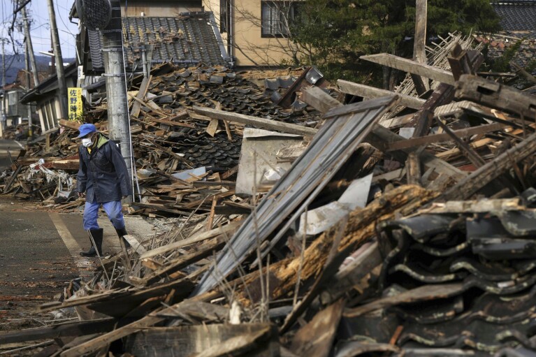 A man walks between collapsed houses in Suzu, Ishikawa prefecture, Japan Friday, Jan. 5, 2024. Monday’s temblor decimated houses, twisted and scarred roads and scattered boats like toys in the waters, and prompted tsunami warnings. (Kyodo News via AP)