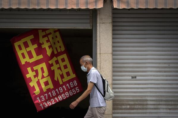 A man wearing a face mask walks by a banner that reads "Prosperous shop for rent" hangs on a vacant shop lot in Beijing, Wednesday, Aug. 17, 2022. Factories in China's southwest have shut down after reservoirs used to generate hydropower ran low in a worsening drought, adding to economic strains at a time when President Xi Jinping is trying to extend his position in power. (AP Photo/Andy Wong)