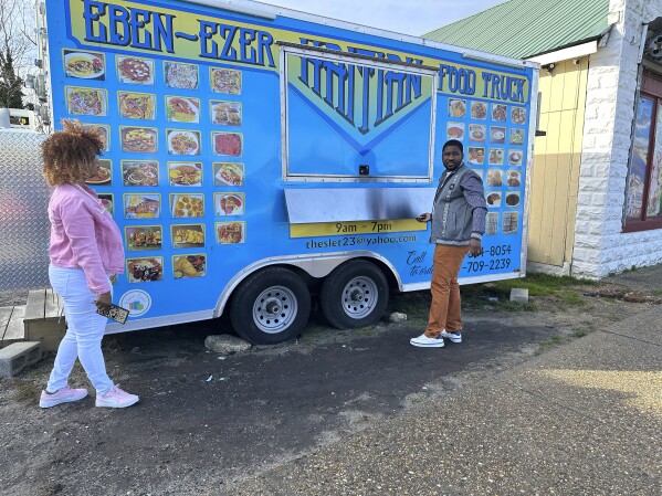 Clemene Bastien and Theslet Benoir stand outside of their Eben-Ezer Haitian food truck in Parksley, Va., on Wednesday, Jan. 24, 2024. The married couple is suing the town in federal court over allegations that their food truck was forced to close. The couple also says a town councilman cut the mobile kitchen's water line and screamed, 