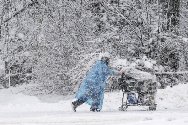 A pedestrian pushes a shopping cart on Cordova Street during a heavy snowfall, Thursday, Nov. 9, 2023 in Anchorage, Alaska. Four homeless people have died in Anchorage in the last week, underscoring the city’s ongoing struggle to house a large houseless population at the same time winter weather has returned, with more than 2 feet (0.61 meters) of snow falling within 48 hours. (Marc Lester/Anchorage Daily News via AP)