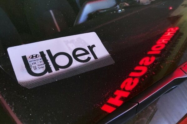 File - An Uber sign is displayed inside a car in Glenview, Ill., on Dec. 17, 2022. Ride-hailing companies Uber and Lyft will pay a combined $328 million to settle wage theft claims in New York, Attorney General Letitia James announced Thursday. (AP Photo/Nam Y. Huh, File)