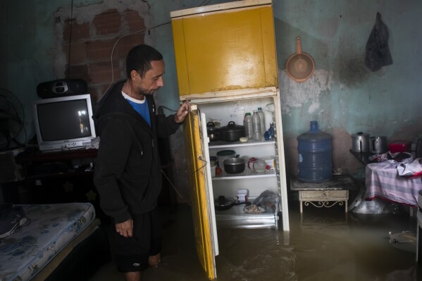 Nicelio Goncalves opens the fridge at his flooded home after heavy rains in Duque de Caxias, Brazil, Sunday, March 24, 2024. (AP Photo/Bruna Prado)