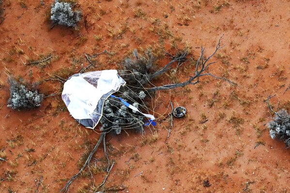 In this photo provided by the Japan Aerospace Exploration Agency (JAXA), a capsule, center, dropped by Hayabusa2 is seen before being retrieved in Woomera, southern Australia, Sunday, Dec. 6, 2020. A Japanese capsule carrying the first samples of asteroid subsurface shot across the night atmosphere early Sunday before successfully landing in the remote Australian Outback, completing a mission to provide clues to the origin of the solar system and life on Earth. (JAXA via AP)