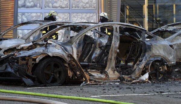 A burnt-out Tesla sits in front of a Tesla dealership early Saturday, March 29, 2025 in Ottersberg, Germany.  (J'rn H'neke/dpa via AP)