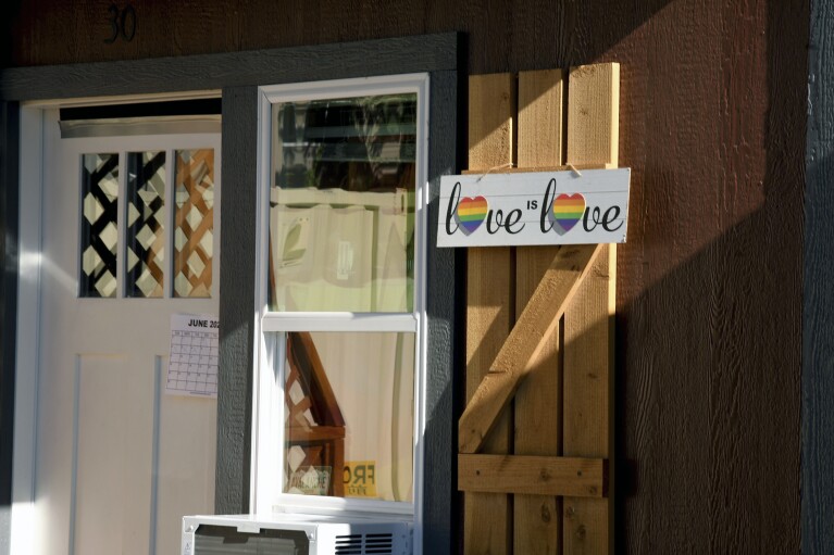 A Love is Love sign is displayed at a micro community in Denver on Wednesday, June 5, 2024. The communities consist of small cabin-like structures with a twin bed, desk and closet. The city built three such communities with nearly 160 units total in about six months, at roughly $25,000 per unit to ease homelessness. (AP Photo/Thomas Peipert)