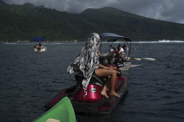 A woman shelters from the sun as she watches surfers catch waves in Vailao, Tahiti, French Polynesia, Monday, Jan. 15, 2024. (AP Photo/Daniel Cole)