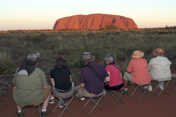 FILE - In this April 22, 2014, file photo, people sit on camp chairs at a popular viewing point to watch the sunset on Uluru, Australia. A climbing ban from late Friday, Oct. 25, 2019 on the sandstone monolith called Uluru that dominates Australia’s arid center marks indigenous Australians finding a new voice in national decision-making. The rock has long been celebrated as a prized peak to conquer and a sacred site to be revered, but with the ban, the pendulum is swinging decisively toward the rock’s cultural significance to its traditional owners. (AP Photo/Rob Griffith, File)
