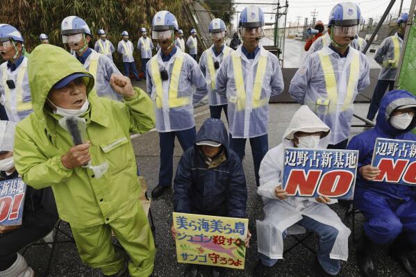 Protesters rally near a gate of Camp Schwab, a U.S. Marine Corps camp, in the Henoko neighborhood of Nago, northeast of Okinawa, Japan, Wednesday, Dec. 20, 2023. Signs read, "No new Henoko base." A Japanese court on Wednesday, Dec. 20, 2023, ordered the governor of Okinawa to approve the central government's modified plan for landfill work at the planned relocation site of a key U.S. military base on the southern island despite persistent opposition and protests by residents. (Kyodo News via AP)