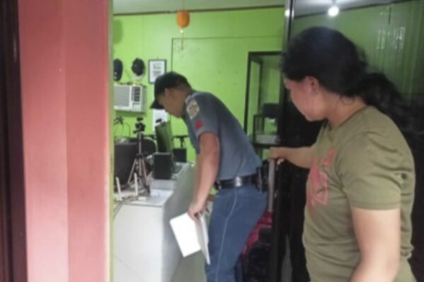 In this handout photo provided by the Calamba Municipal Police Station, a policeman, left, checks on the area where a radio anchor was fatally shot by a man inside his home-based station in Calamba town in Misamis Occidenta province, southern Philippines on Sunday Nov. 5, 2023. A radio anchor was fatally shot by a man inside his southern Philippine station Sunday in a brazen attack that was witnessed by people watching the program live on Facebook. (Calamba Municipal Police Station via AP)